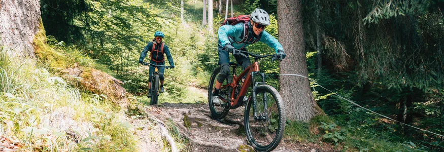 Zwei Mountainbiker fahren auf einem wurzeligen Waldweg bergab