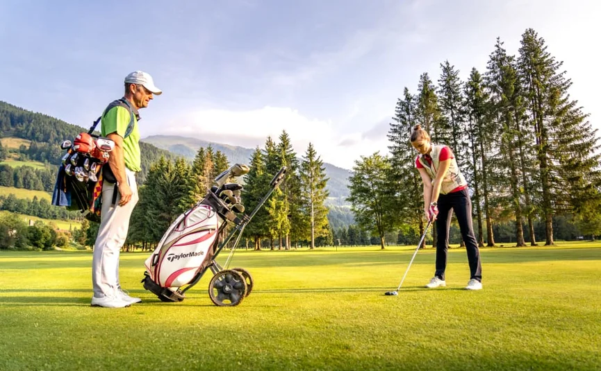 Golf days deluxe / 3 nights Two golfers on a green golf course with mountains and trees in the background