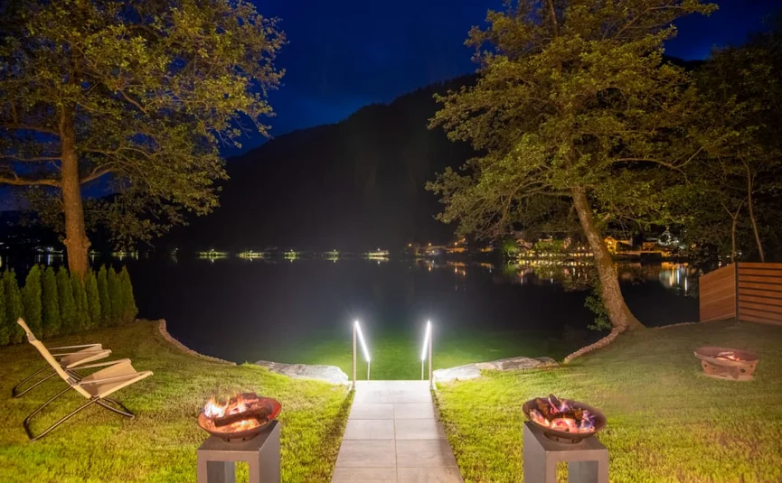 Lit pathway to lakeside with fire pits and chairs at night