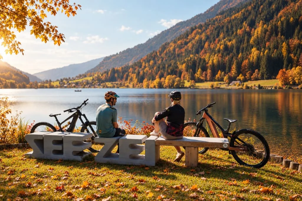 Family Herbst Auszeit 5=4 Twee fietsers zitten met hun mountainbikes aan een meer, met herfstkleurige bergen op de achtergrond