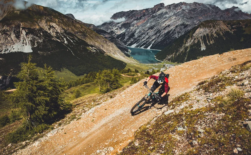 Mountain biker riding on mountain trail with lake and mountains behind