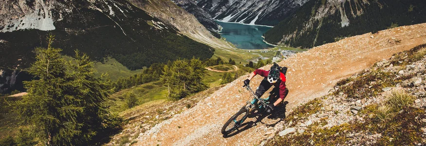 Livigno © Livigno - Ezequiel Urrets Mountainbiker op bergpad met meer en bergen op de achtergrond