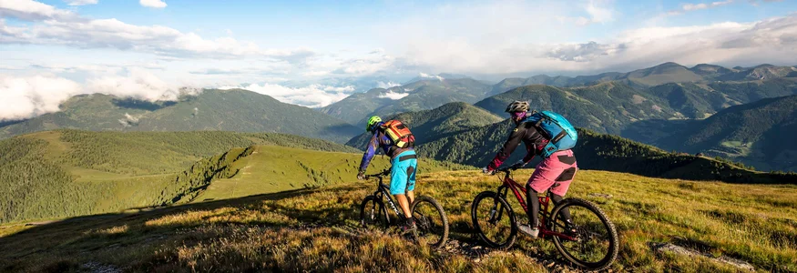 Two mountain bikers riding on a trail with a panoramic mountain view