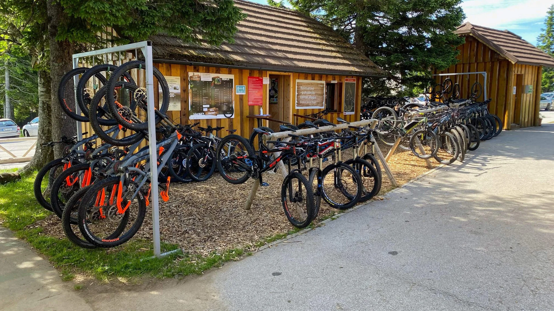 Fahrradverleihstation mit vielen Mountainbikes vor Holzhütten unter Bäumen