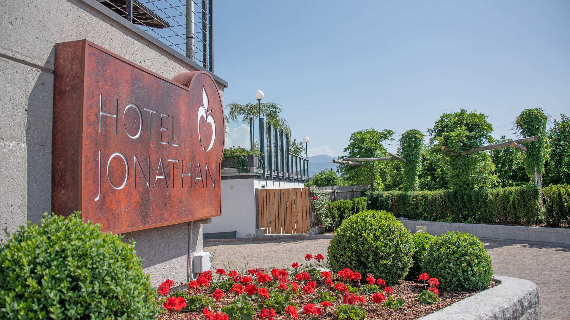 Eingangsschild des Hotel Jonathan mit Garten und rotem Blumenschmuck