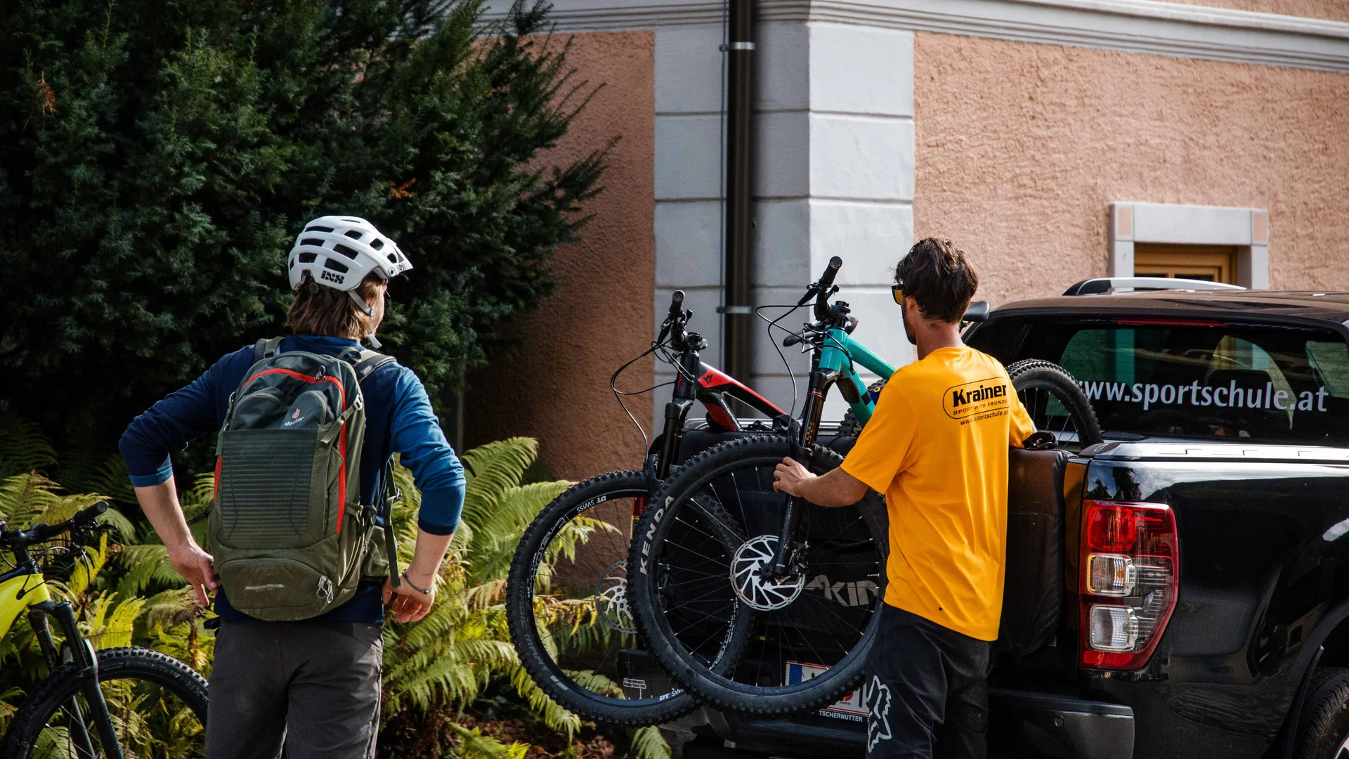 Zwei Männer laden Mountainbikes auf einen schwarzen Pickup