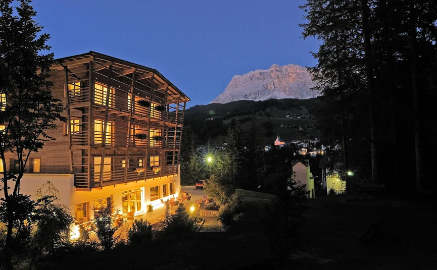 Beleuchtetes Holzhaus bei Nacht in Alpenlandschaft mit Berg im Hintergrund