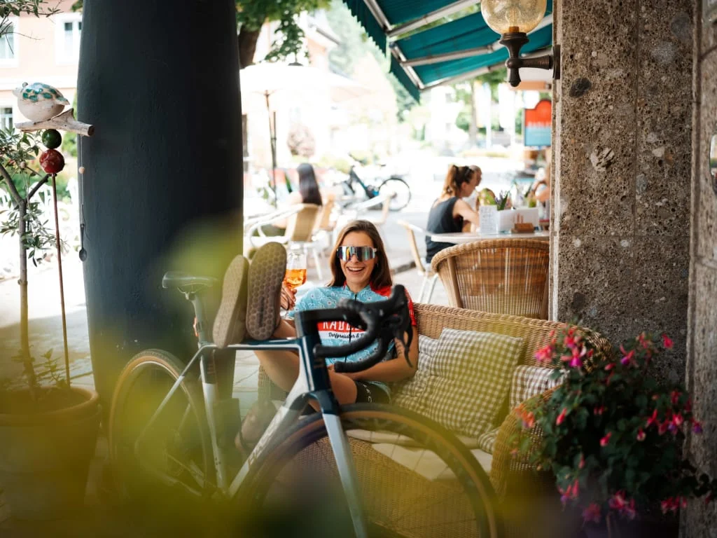 Frau entspannt mit Fahrrad und Getränk in einem Café im Freien
