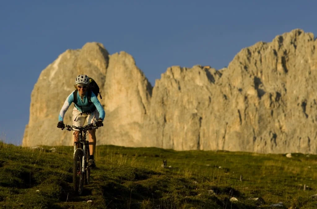 Vrouw mountainbiken op grasachtig pad met rotsachtige bergen op de achtergrond