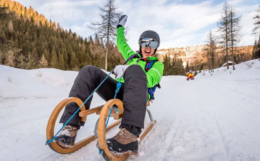 Ski, Gourmet & Dorfsilvester Persoon met helm en skibril op een houten slee in een besneeuwd berglandschap