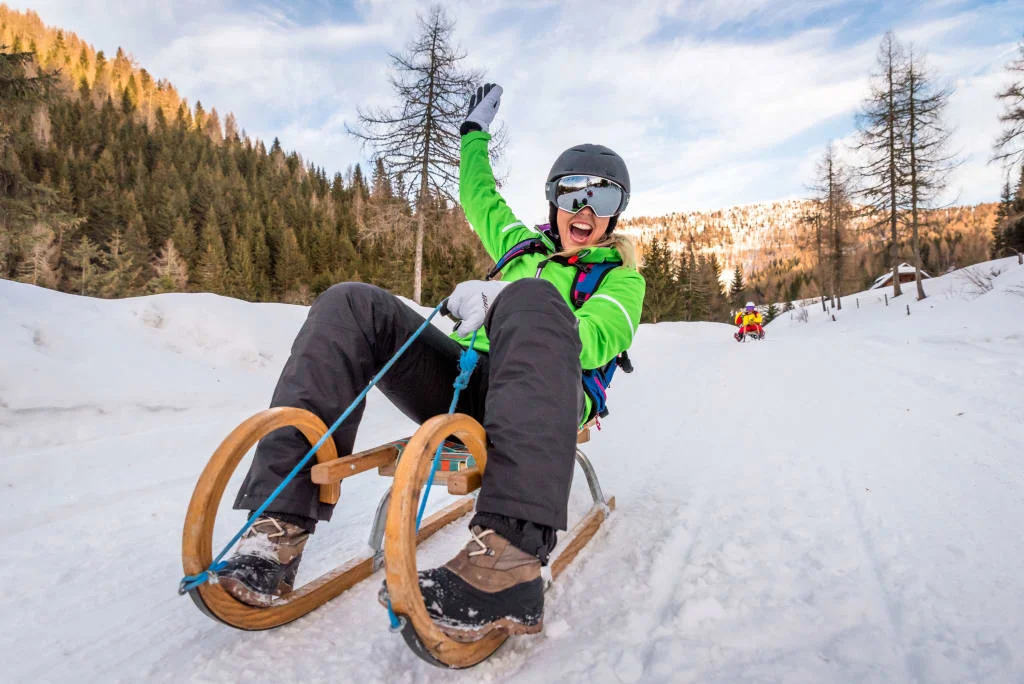 Ski, Gourmet & Dorfsilvester Persoon met helm en skibril op een houten slee in een besneeuwd berglandschap