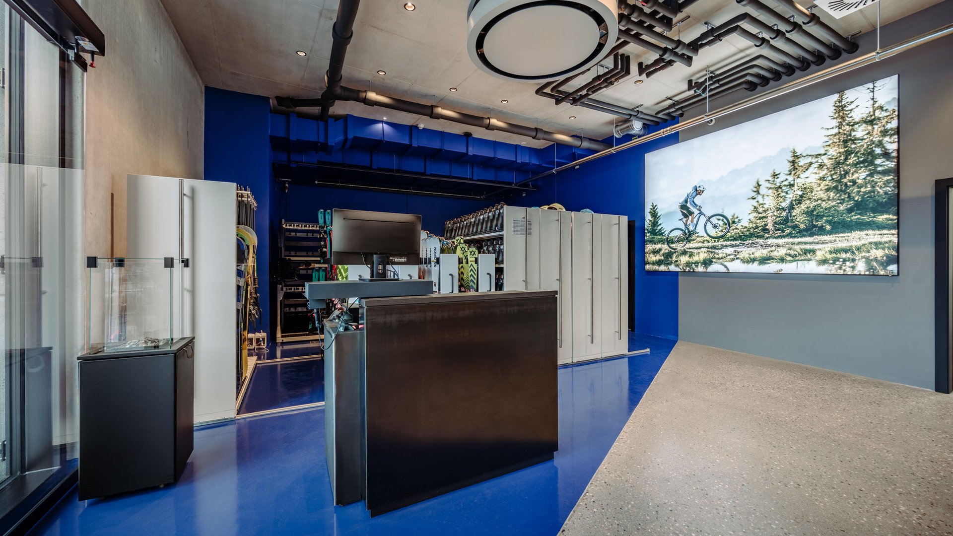 MTB in der DNA: Bikesommer im DIPS&DROPS © Matthias Warter Moderne Sportartikelstation mit Skiern und Fahrradbild an der Wand