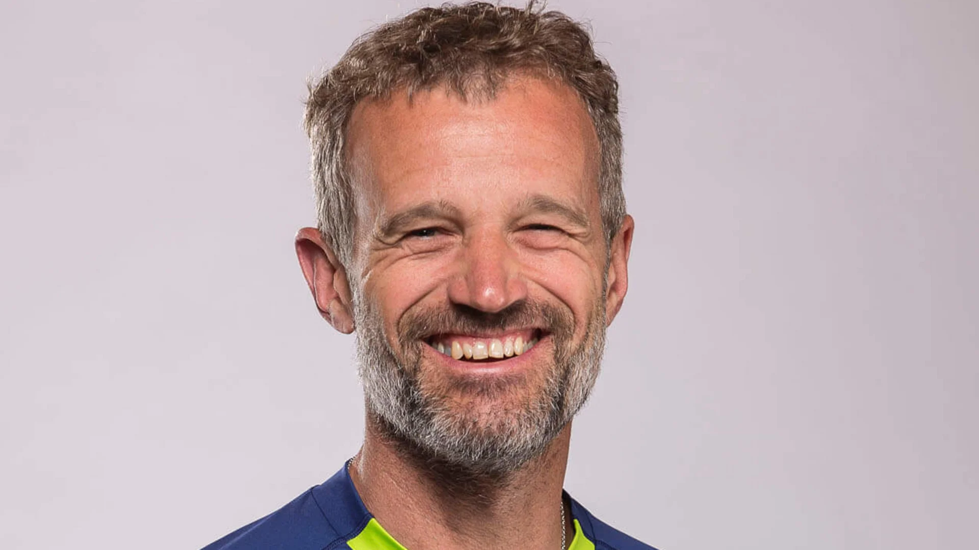 Mann lächelt in blau-grünem Mountainbike-Trikot vor grauem Hintergrund