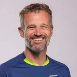 Mann lächelt in blau-grünem Mountainbike-Trikot vor grauem Hintergrund