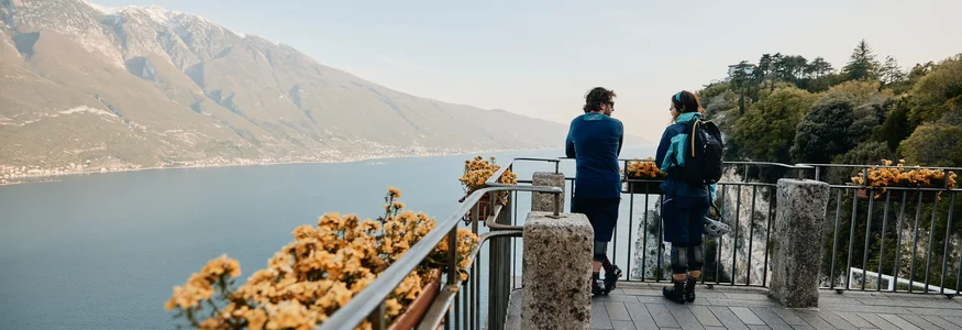 Zwei Menschen auf Aussichtspunkt mit Blick auf See und Berge