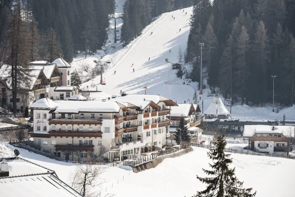 Verschneites Skigebiet mit Ski fahrern und Gebäuden vor Wald im Hintergrund