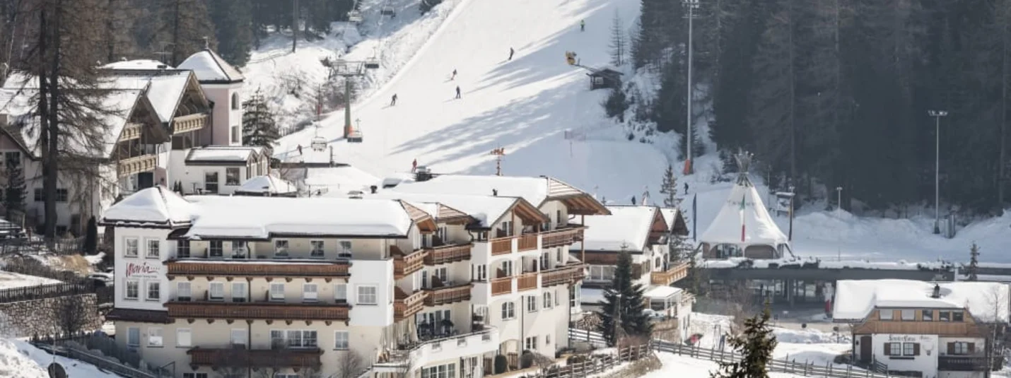 Familien-Sonnen-Skitage 7=6 Verschneites Skigebiet mit Ski fahrern und Gebäuden vor Wald im Hintergrund