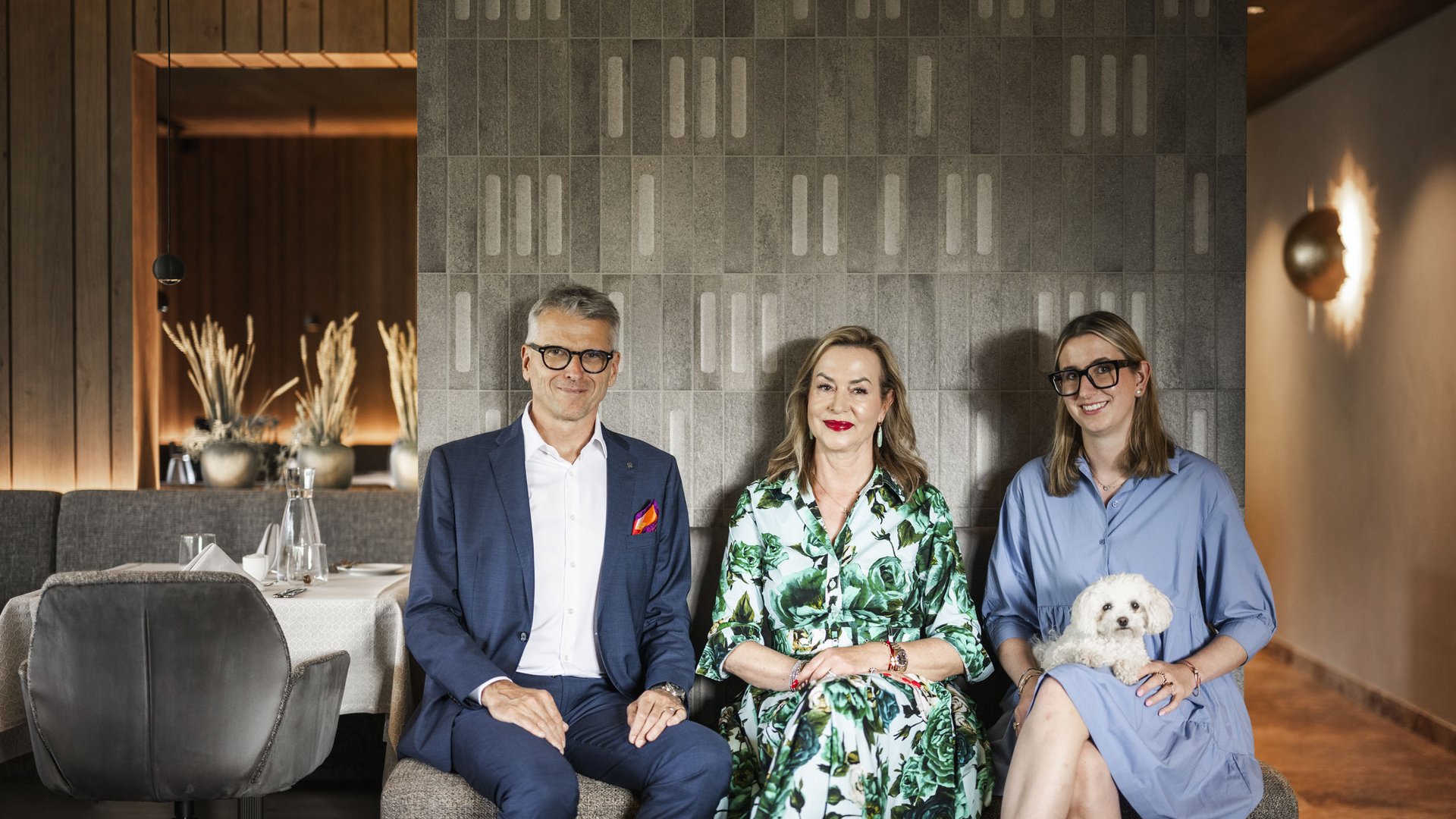 Mountainbike-Saisonstart am Kronplatz © Hannes Niederkofler Drei Personen sitzen nebeneinander, eine hält einen kleinen weißen Hund auf dem Schoß