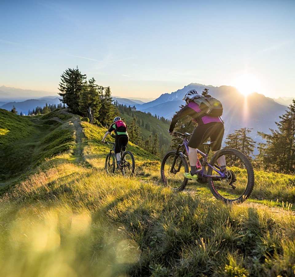Bike & Taste die Salzburger Sportwelt © Salzburger Sportwelt - Andreas Meyer Zwei Mountainbiker fahren auf einem Bergpfad bei Sonnenuntergang