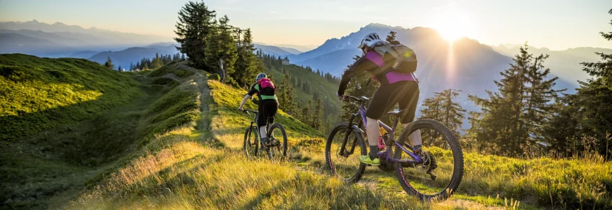 Zwei Mountainbiker fahren auf einem Bergpfad bei Sonnenuntergang