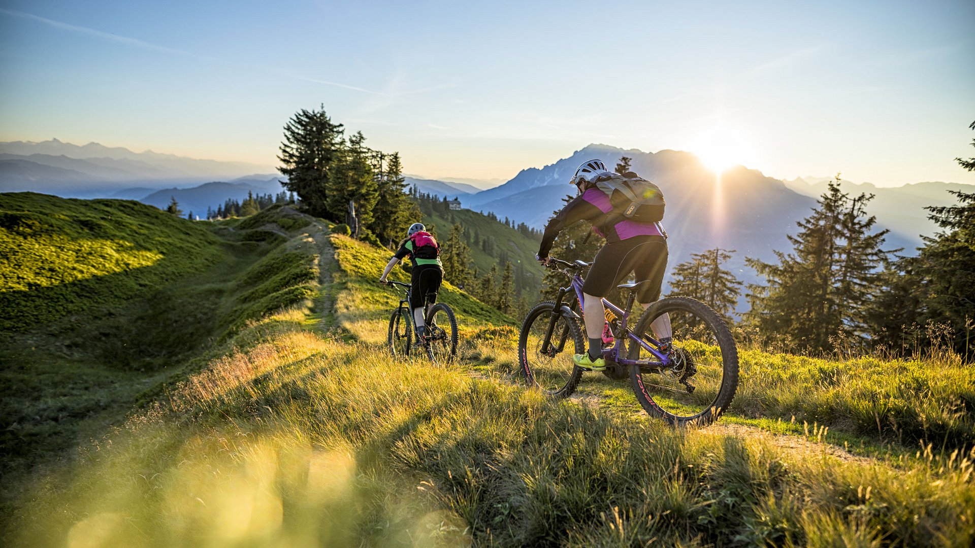 Zwei Mountainbiker fahren auf einem Bergpfad bei Sonnenuntergang