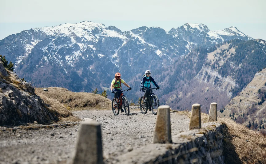 Zwei Radfahrer fahren auf bergigem Weg mit schneebedeckten Bergen im Hintergrund