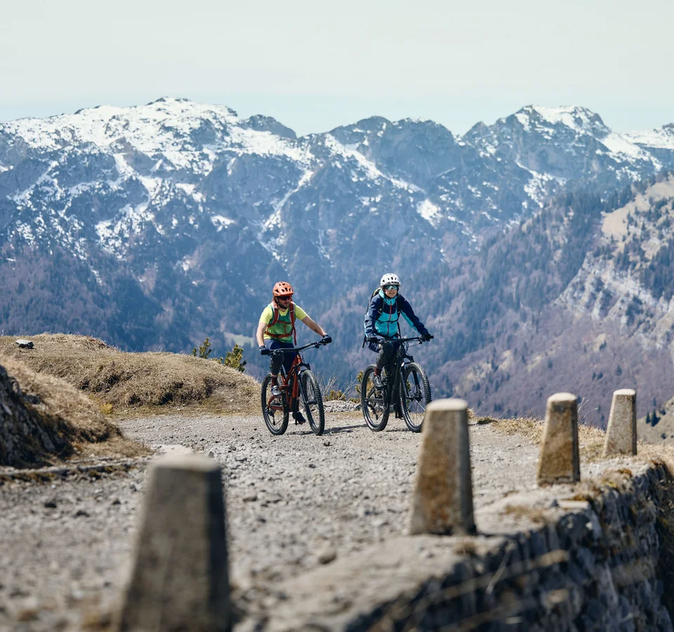 Zwei Radfahrer fahren auf bergigem Weg mit schneebedeckten Bergen im Hintergrund