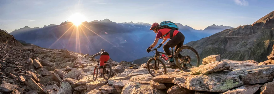 Two mountain bikers riding rocky trail at sunset in the mountains