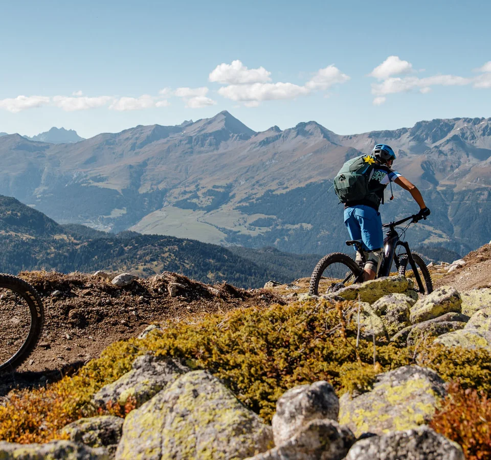Zwei Mountainbiker fahren auf einem Bergpfad mit Alpen im Hintergrund