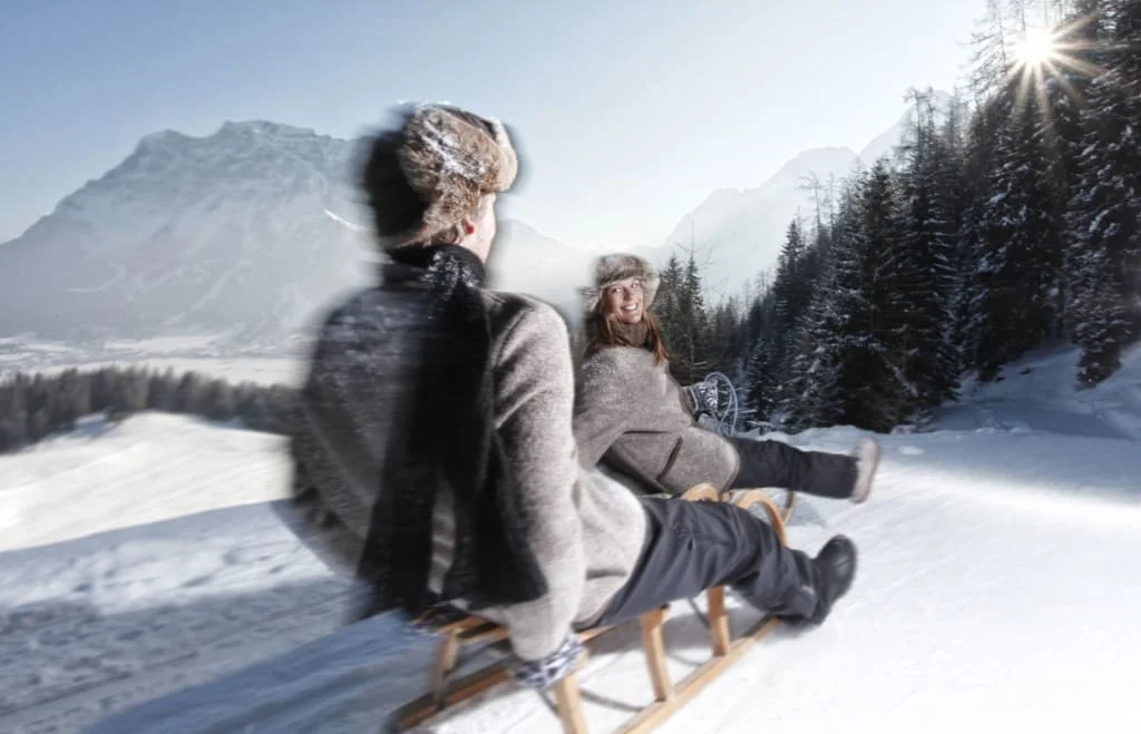 Schönruh Spezial-Skiwochen 6=7 Tage Winter 2027 ohne Skipass Zwei Personen rodeln im Winter mit Schnee und Bergen im Hintergrund