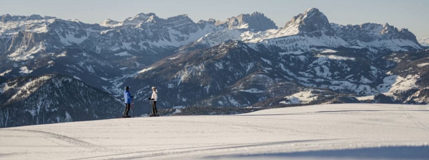 Ladin Winter Days - zwischen Ski & Tradition 🎭 Twee skiërs op een besneeuwde vlakte met besneeuwde bergen op de achtergrond
