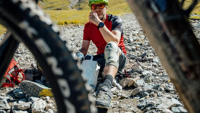 Mountainbiker sitzt auf steinigem Weg und macht Pause