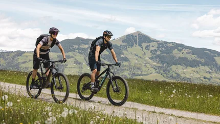 Zwei Mountainbiker fahren auf einem Weg in den Alpen bei sonnigem Wetter
