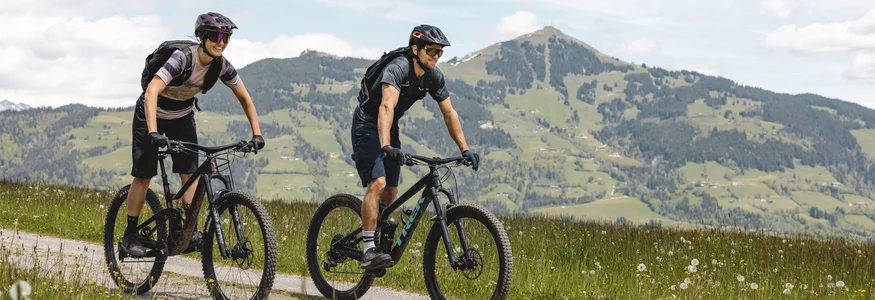 Zwei Mountainbiker fahren auf einem Weg in den Alpen bei sonnigem Wetter