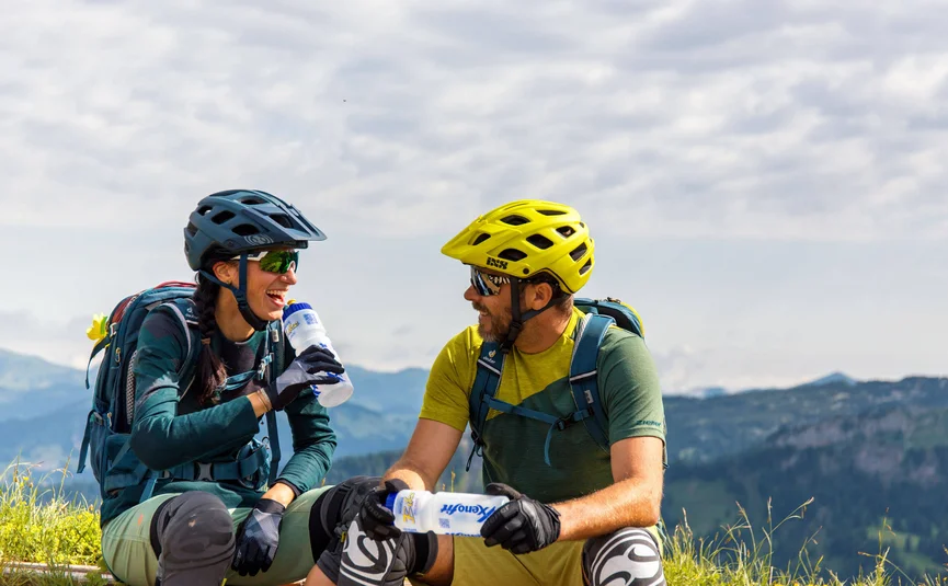 Twee fietsers lachen tijdens pauze op een bergweide met drinkflessen