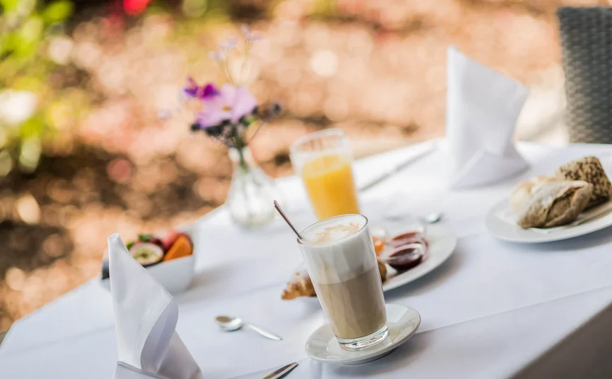 Latte macchiato, orange juice, rolls and jam on a set table