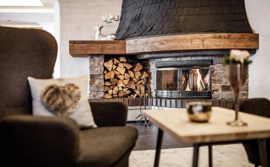 Gemütlicher Raum mit Kamin, Feuerholzstapel und braunem Sessel