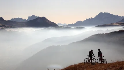 Zwei Mountainbiker auf einem Hügel mit nebligen Bergen im Hintergrund