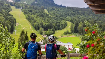 Twee fietsers met helmen en rugzakken kijken uit op groene bergen in een landschap