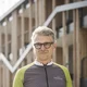 Älterer Mann in Fahrradbekleidung hält Helm vor einem modernen Gebäude