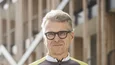 Älterer Mann in Fahrradbekleidung hält Helm vor einem modernen Gebäude