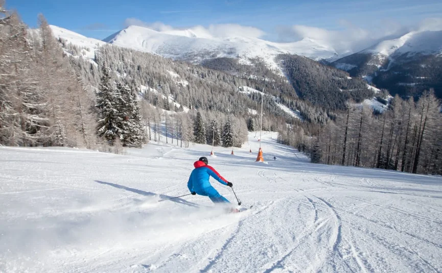 Skier in blue jacket skiing down snowy slope in mountain landscape