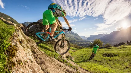 Two mountain bikers descending a steep hill on a sunny day