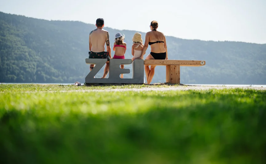 Familie sitzt auf Bank am See hinter Buchstaben ZEIT