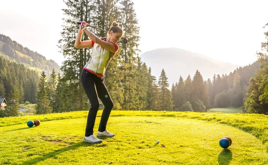 Woman playing golf on green course with mountains and trees in background