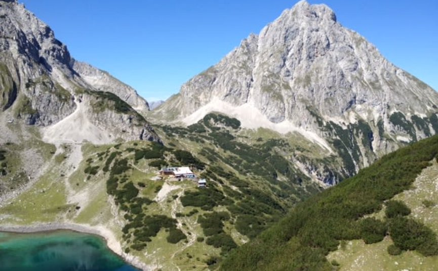 5=4 Tage Zugspitze Bergfrühling Berglandschaft mit klarem See und Berghütte unter blauem Himmel