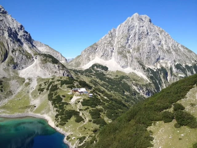 Berglandschaft mit klarem See und Berghütte unter blauem Himmel