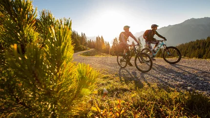 Zwei Mountainbiker fahren auf einem Bergweg bei Sonnenuntergang