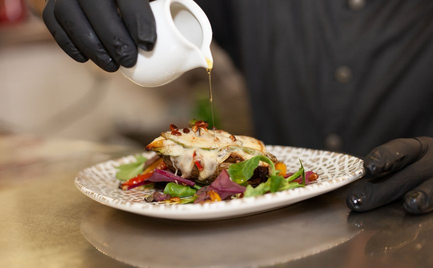 Kok giet olie over een gerecht met kaas en groenten op een bord