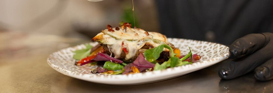 Kok giet olie over een gerecht met kaas en groenten op een bord